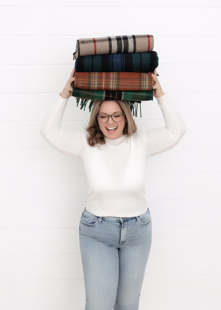 Laura McBride holding folded wool blankets, photographed in a bright, minimal studio setting