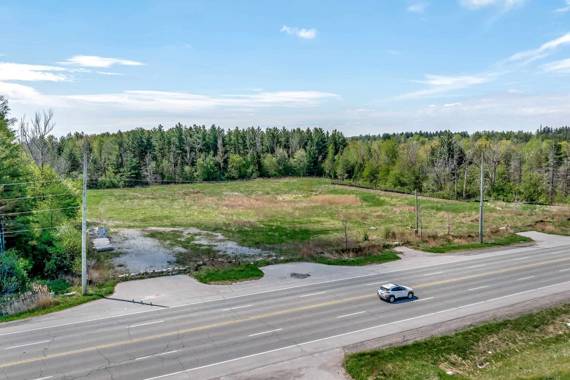 Low aerial view of 3187 Stouffville Road from the south, showing the cleared lot and surrounding tree cover