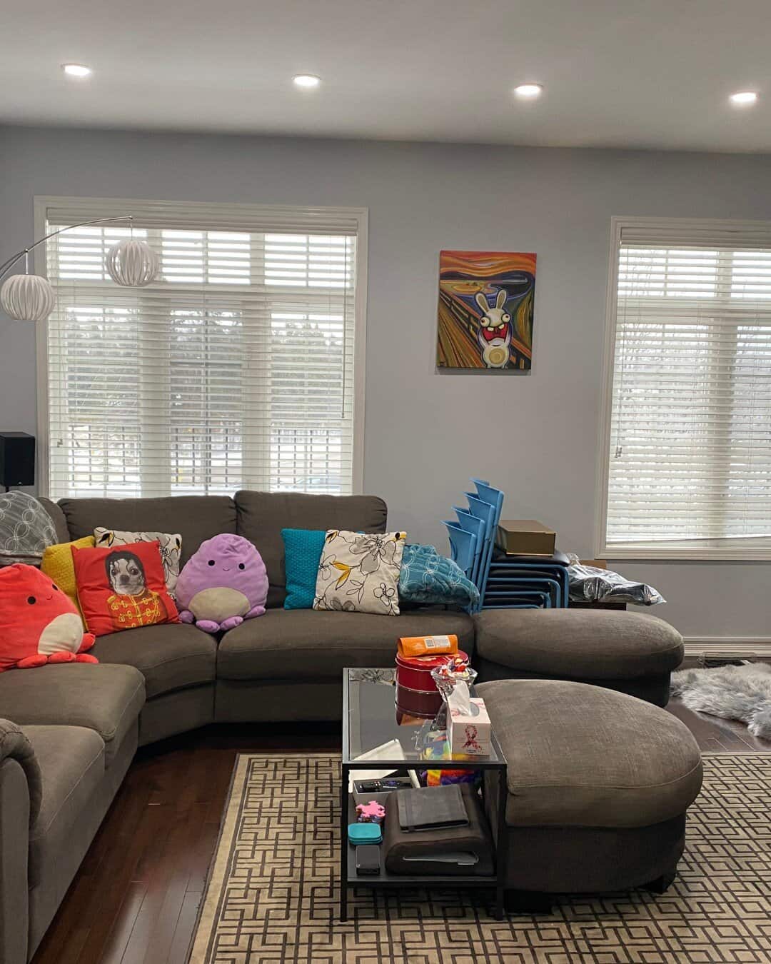 Living room before home staging, with personal items, colourful pillows, and stacked chairs in the corner.