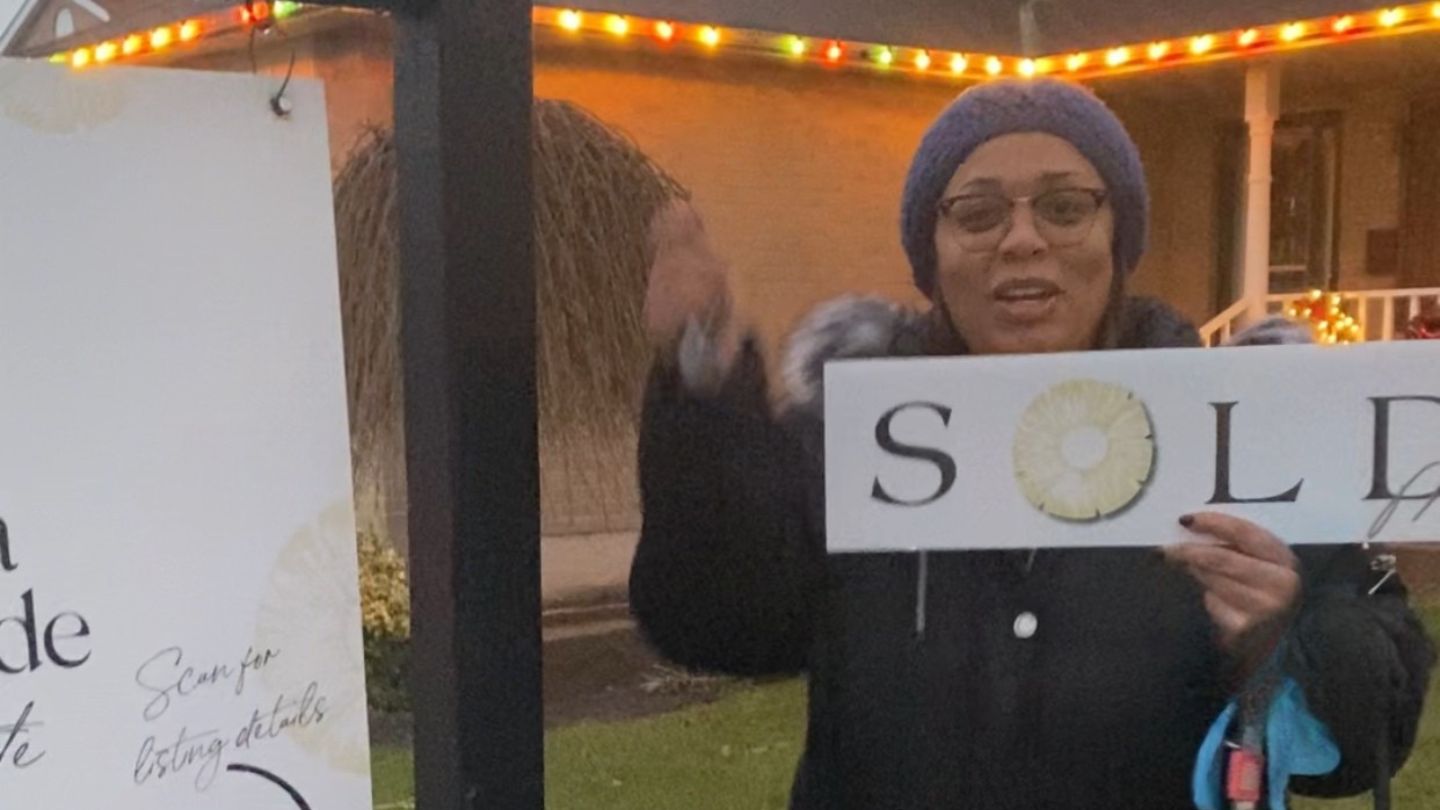 Smiling Ajax homeowner standing outside her sold home at dusk holding a sold sign, celebrating a successful sale with Laura McBride Real Estate.