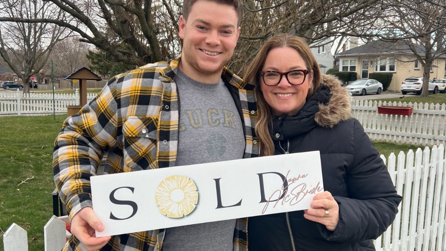 A happy young homeowner stands with Laura McBride REALTOR® after firming up his first home