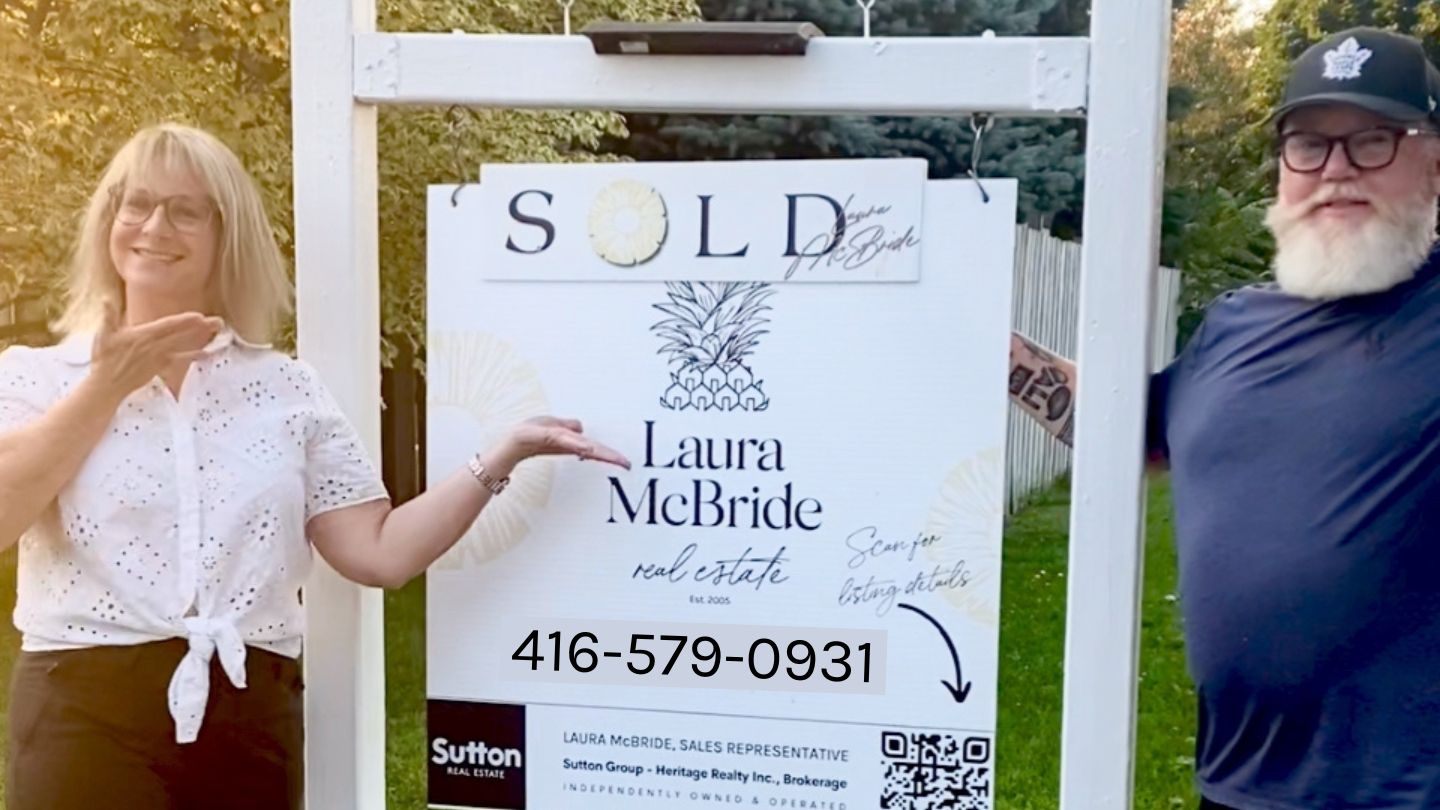 Happy Courtice sellers posing with a SOLD sign beside their Laura McBride Real Estate sign.