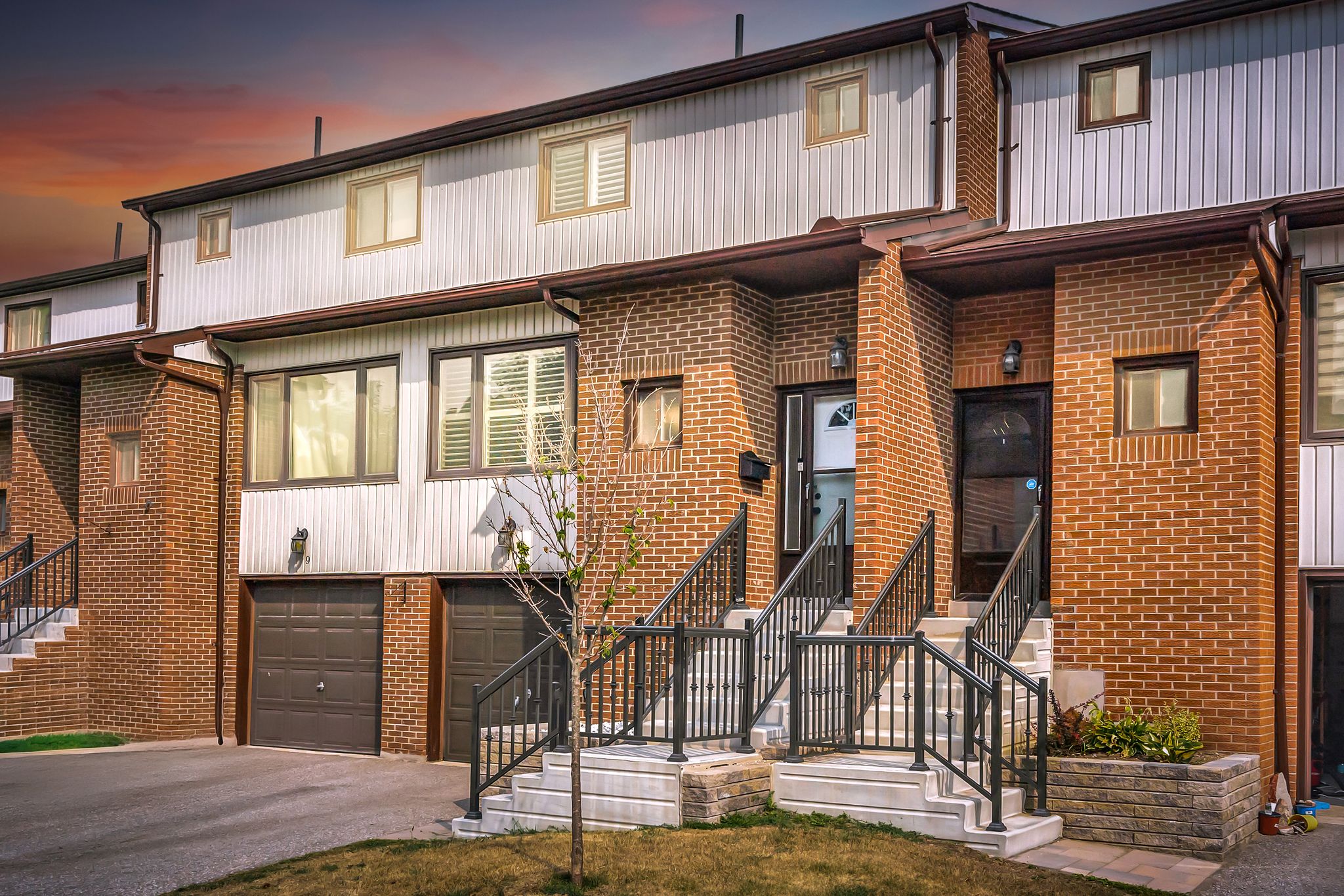 Front exterior view of a renovated red-brick townhouse with a modern black railing and fresh landscaping in Pickering’s West Shore.