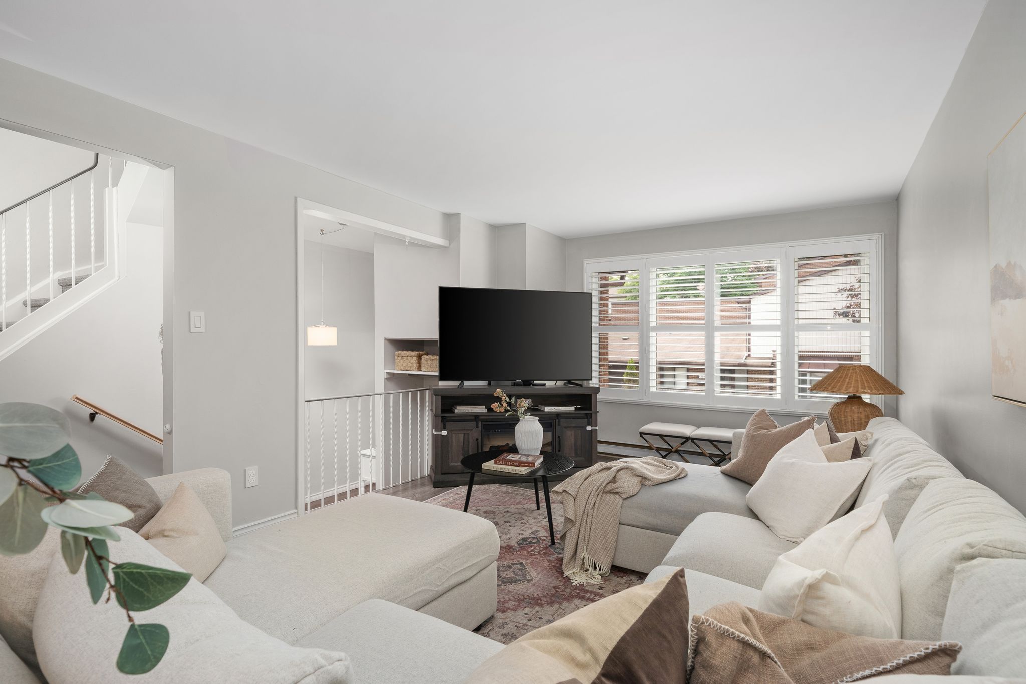 Neutral living room with media console, large TV, and staircases leading to upper and lower levels
