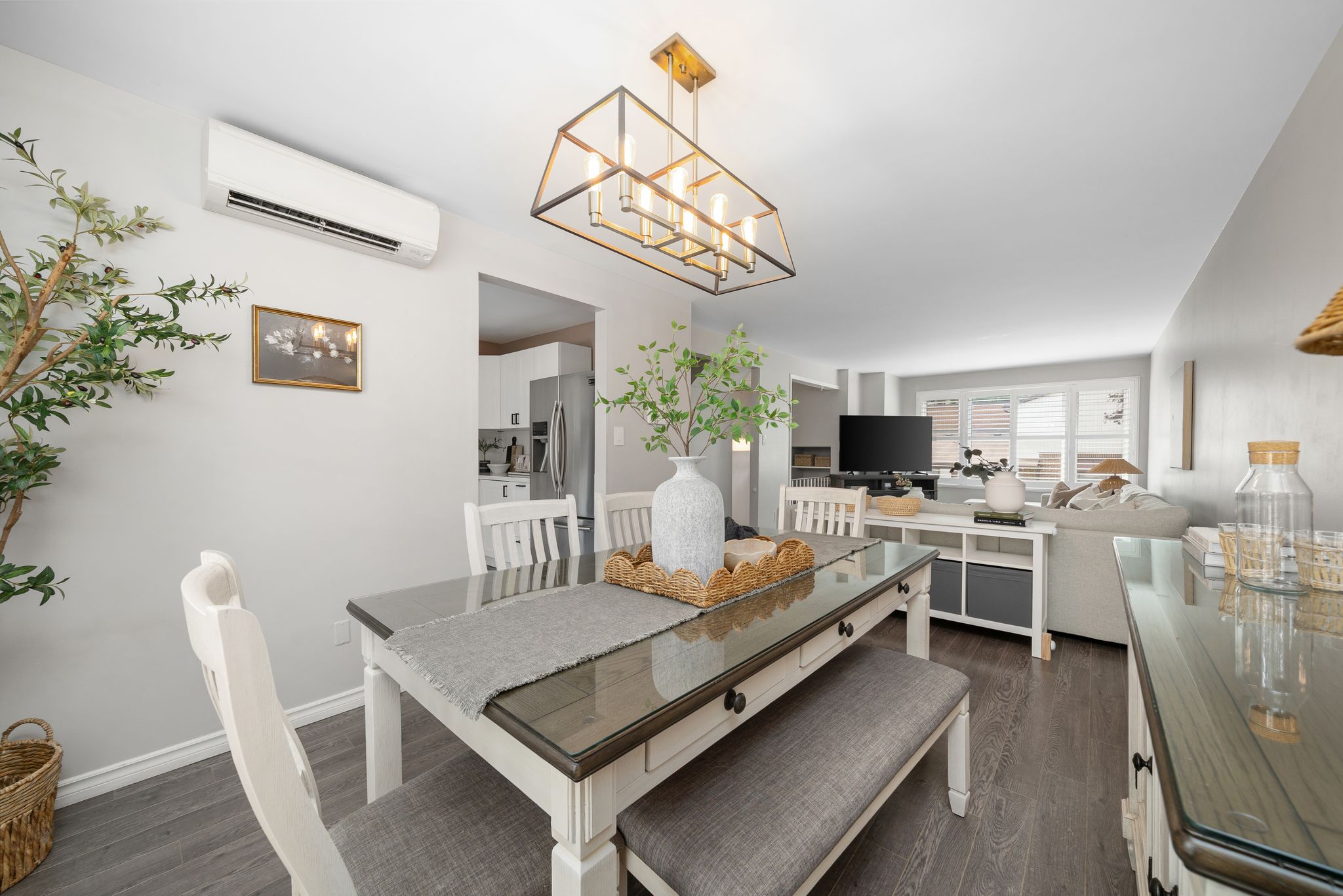 Dining area looking into open-concept living room and kitchen with large windows and neutral design.