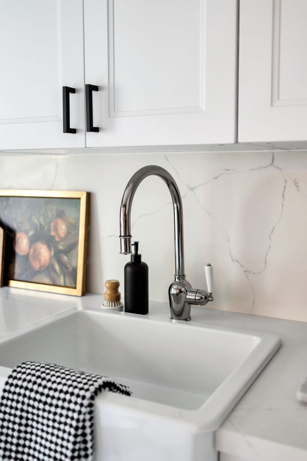 Close-up of white farmhouse sink, chrome faucet, and marble-look backsplash in a modern kitchen.