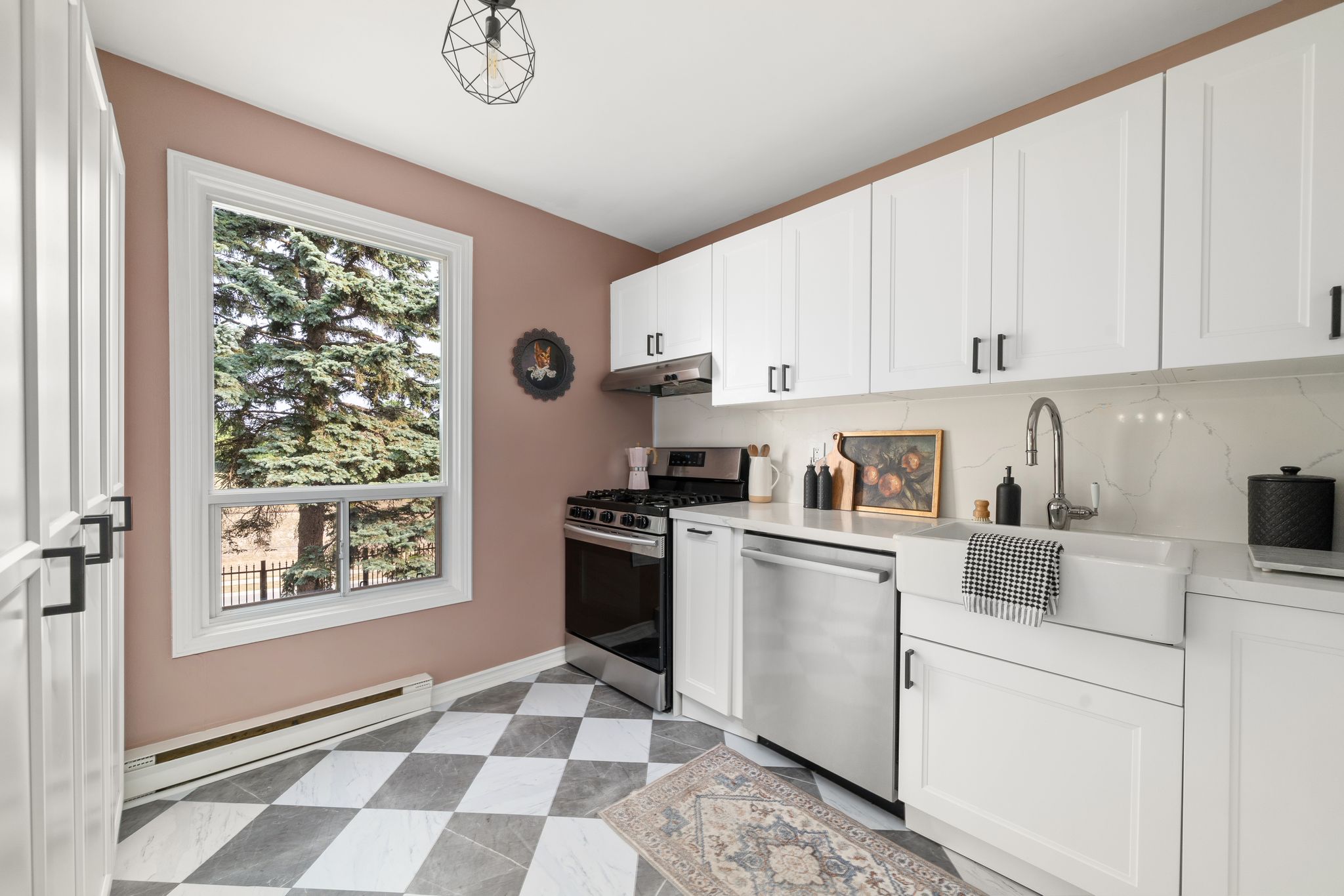 Kitchen window with view of trees, pink accent wall, and full-height pantry cabinetry.