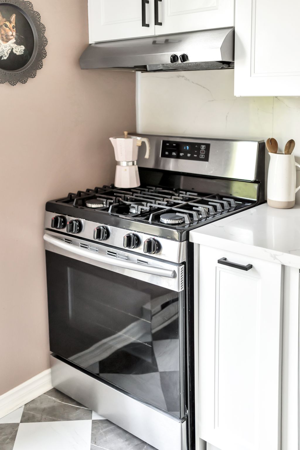 Close-up of a stainless steel gas stove with black cooktop and pink moka pot on quartz countertop.