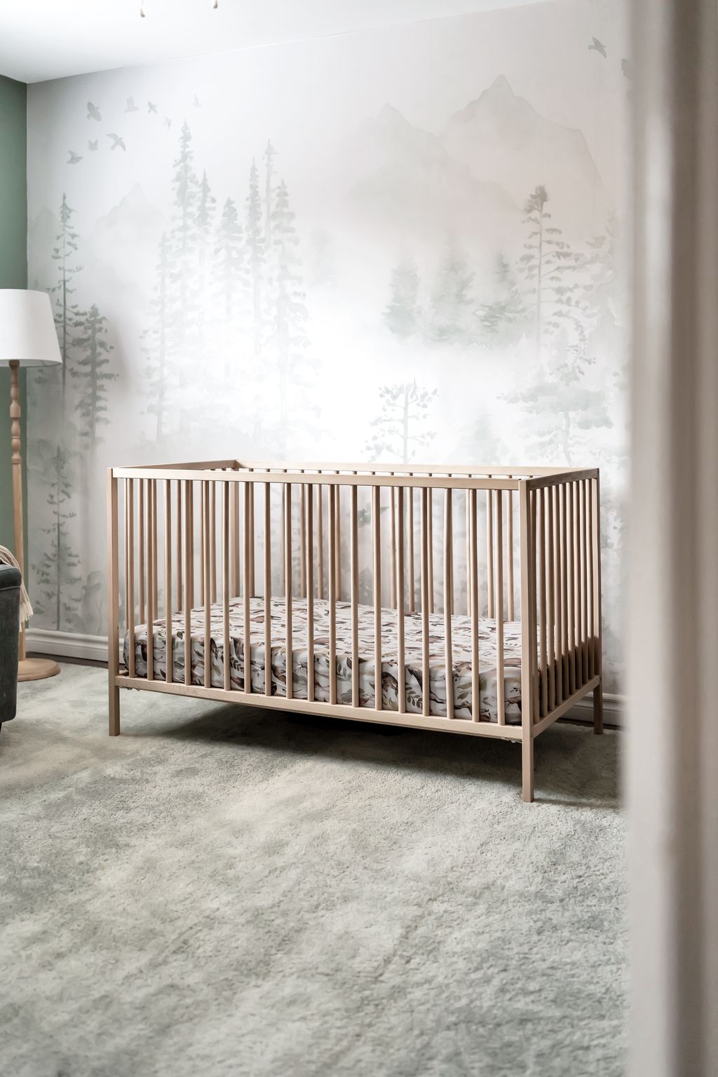 Natural wood crib with forest-themed wallpaper in a nursery