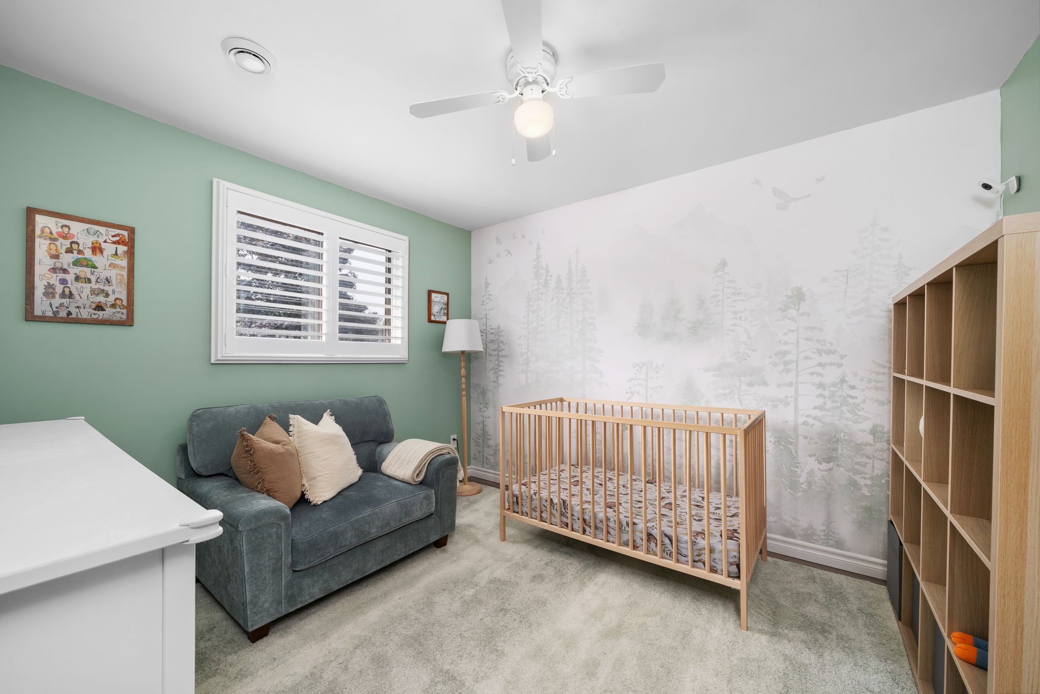 Baby's room with crib, cozy loveseat, built-in shelving, and woodland wallpaper