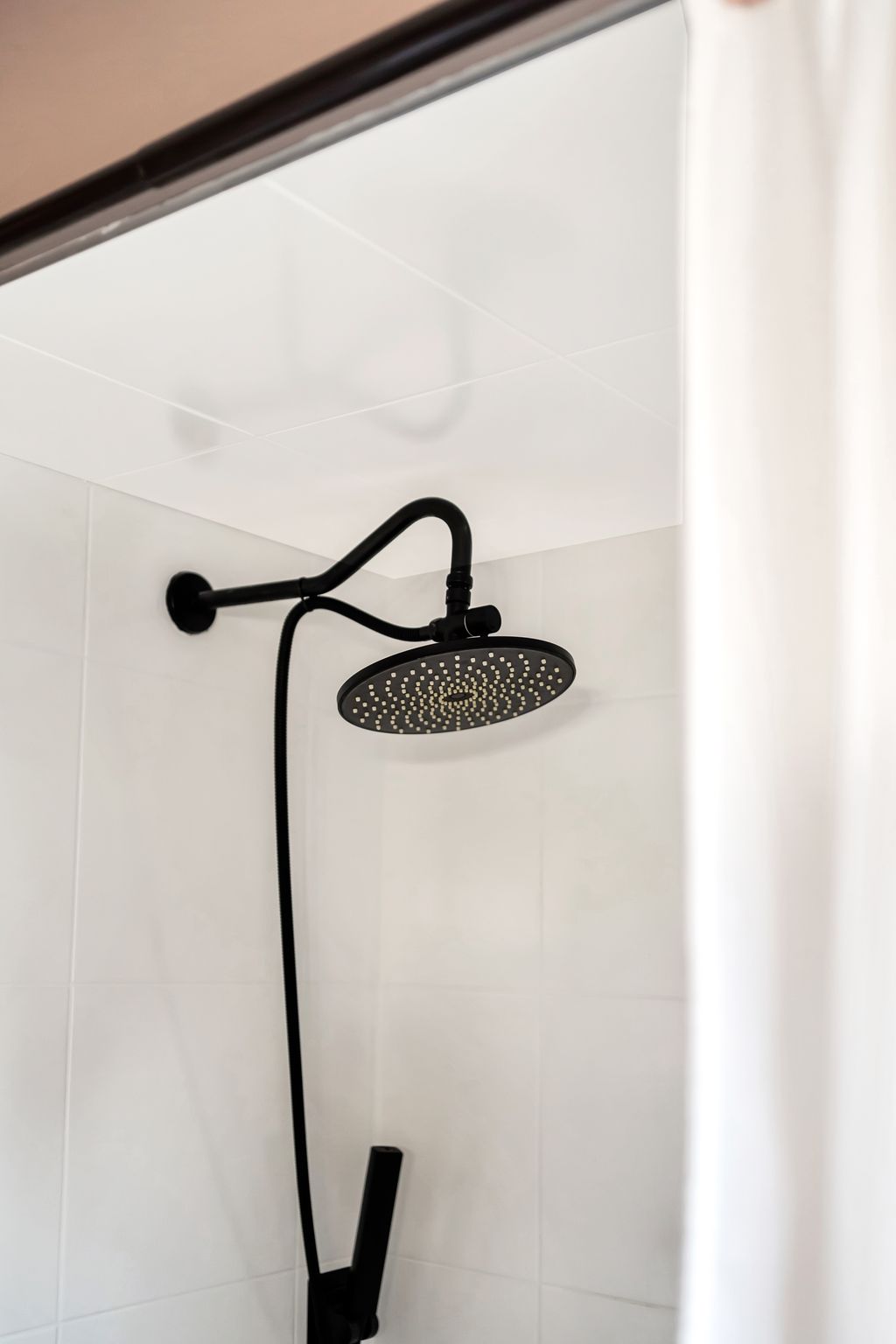 Matte black rain showerhead and handheld combo against clean white tile in renovated bathroom