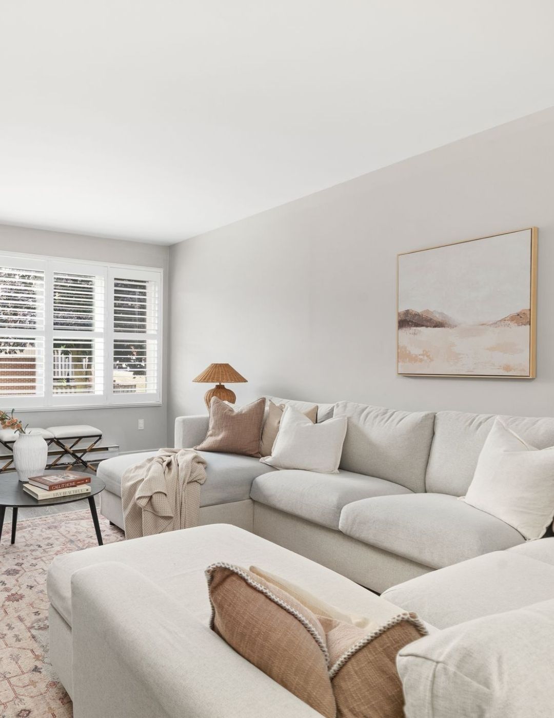 Neutral-toned living room with a large sectional sofa, soft lighting, and California shutters on the front-facing window.