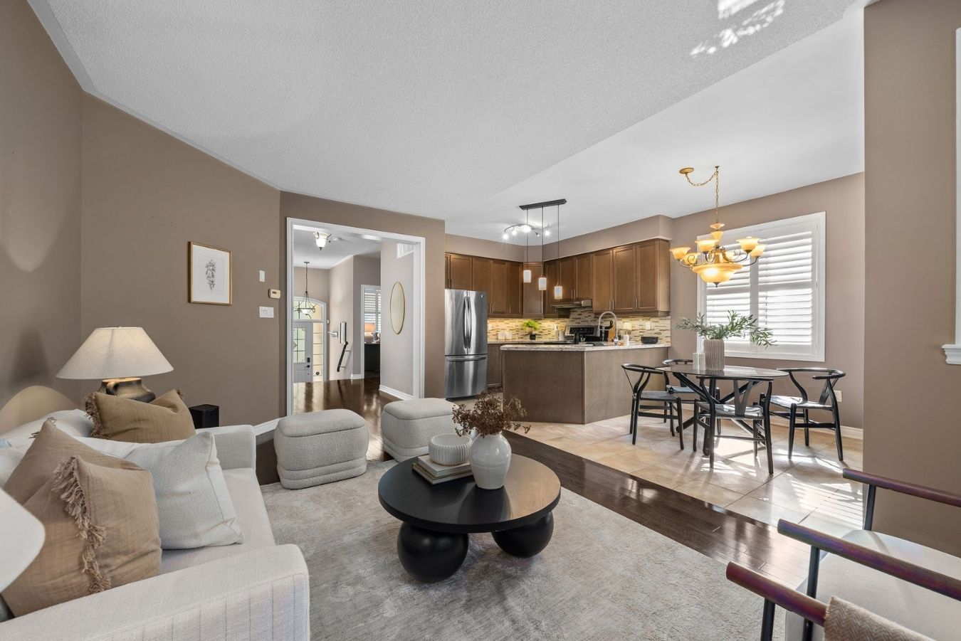 Open-concept living space at 14 Sleepy Hollow Place in Whitby, showing the living room with neutral furnishings, kitchen with maple cabinets and granite counters, and dining area with chandelier lighting.
