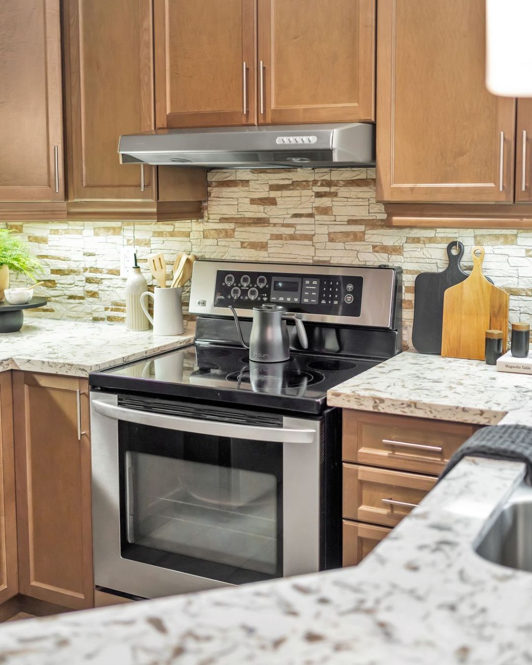 Close-up of the kitchen at 14 Sleepy Hollow Place in Whitby, showing stainless steel stove, maple cabinets, stone tile backsplash, and granite countertops.