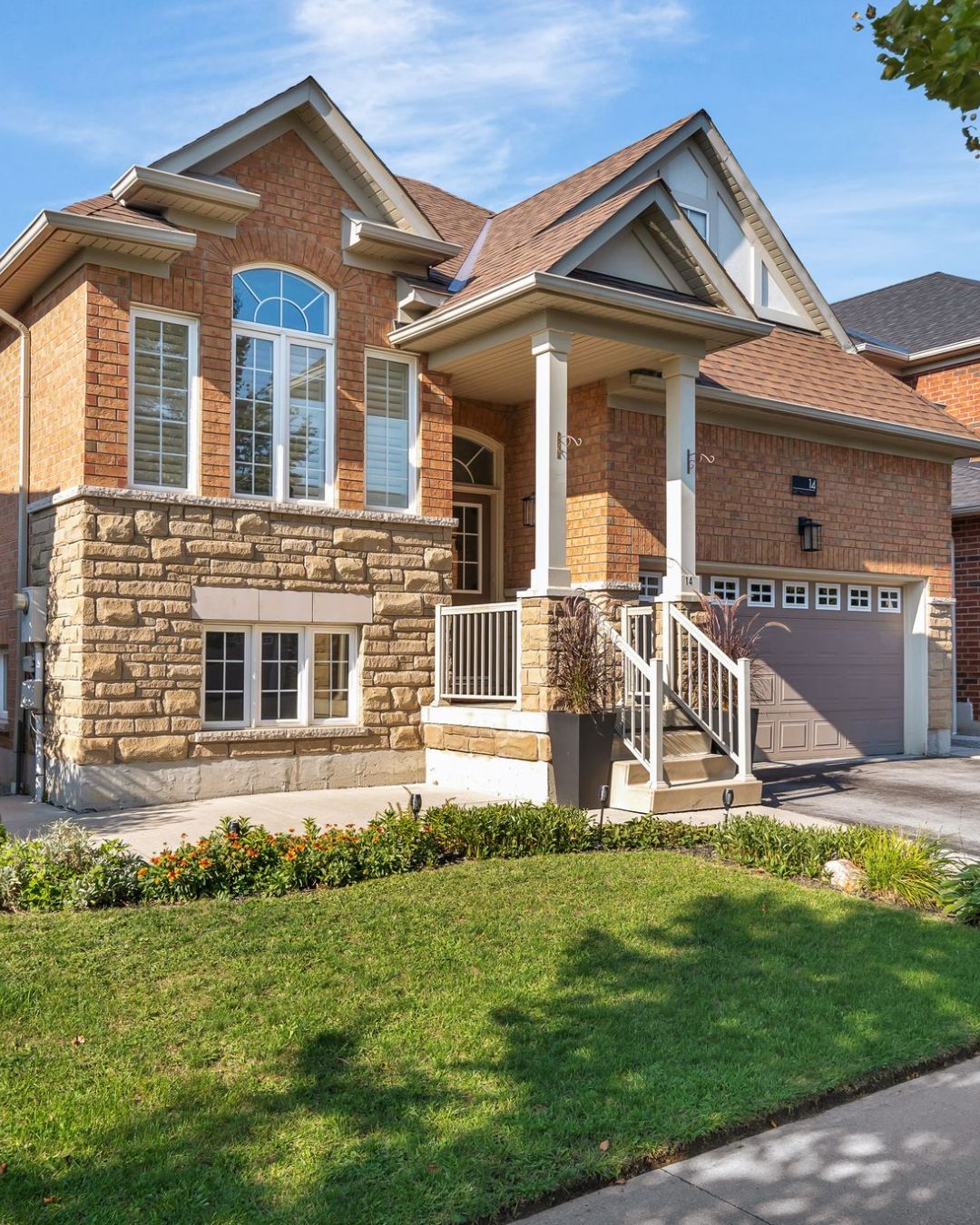 Front exterior view of 14 Sleepy Hollow Place, a raised brick and stone bungalow with a covered porch, double garage, and landscaped front yard, located on a quiet street in Whitby, Ontario.
