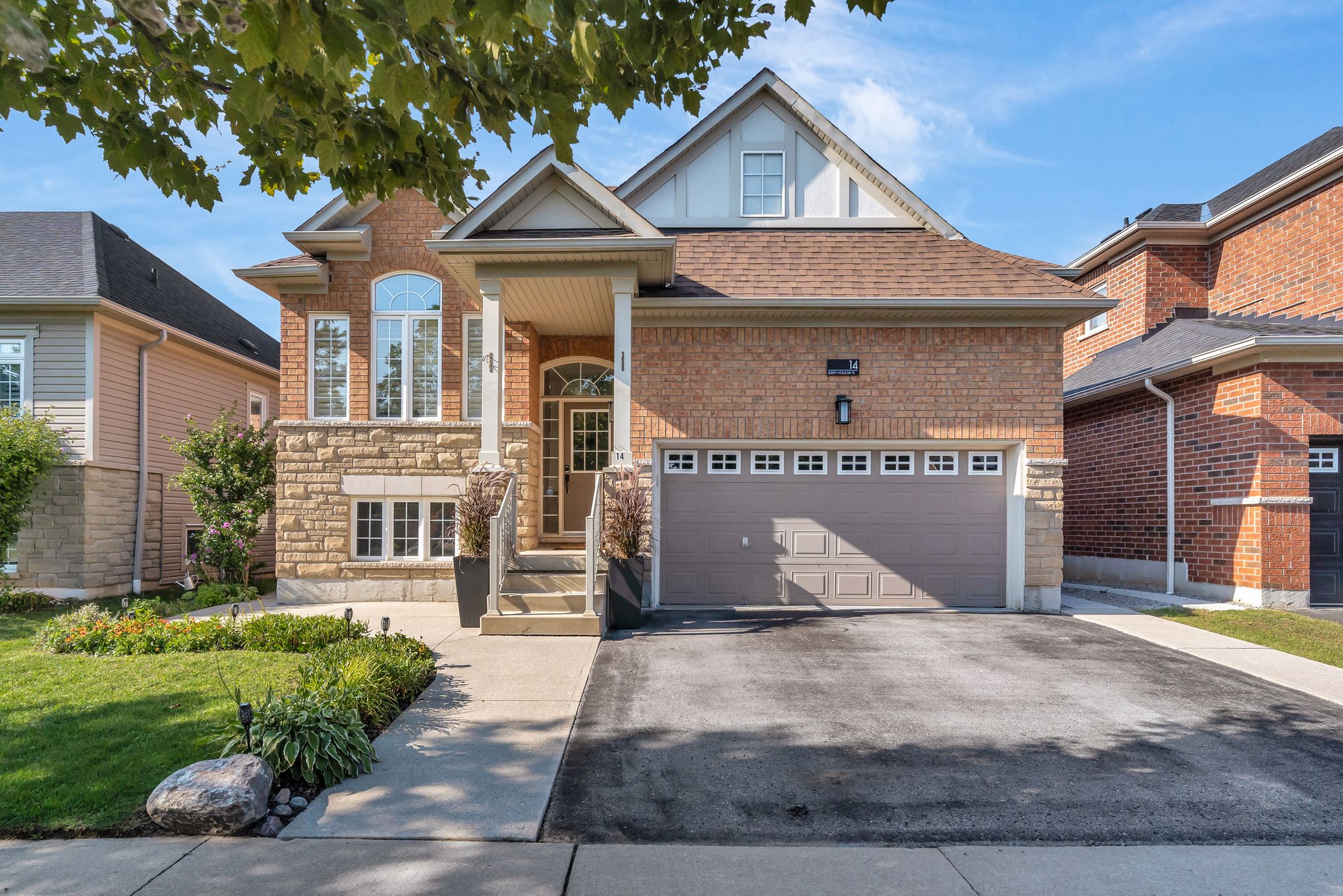 Front view of 14 Sleepy Hollow Place, a raised brick and stone bungalow with double garage, landscaped walkway, and a covered front porch in Whitby, Ontario.