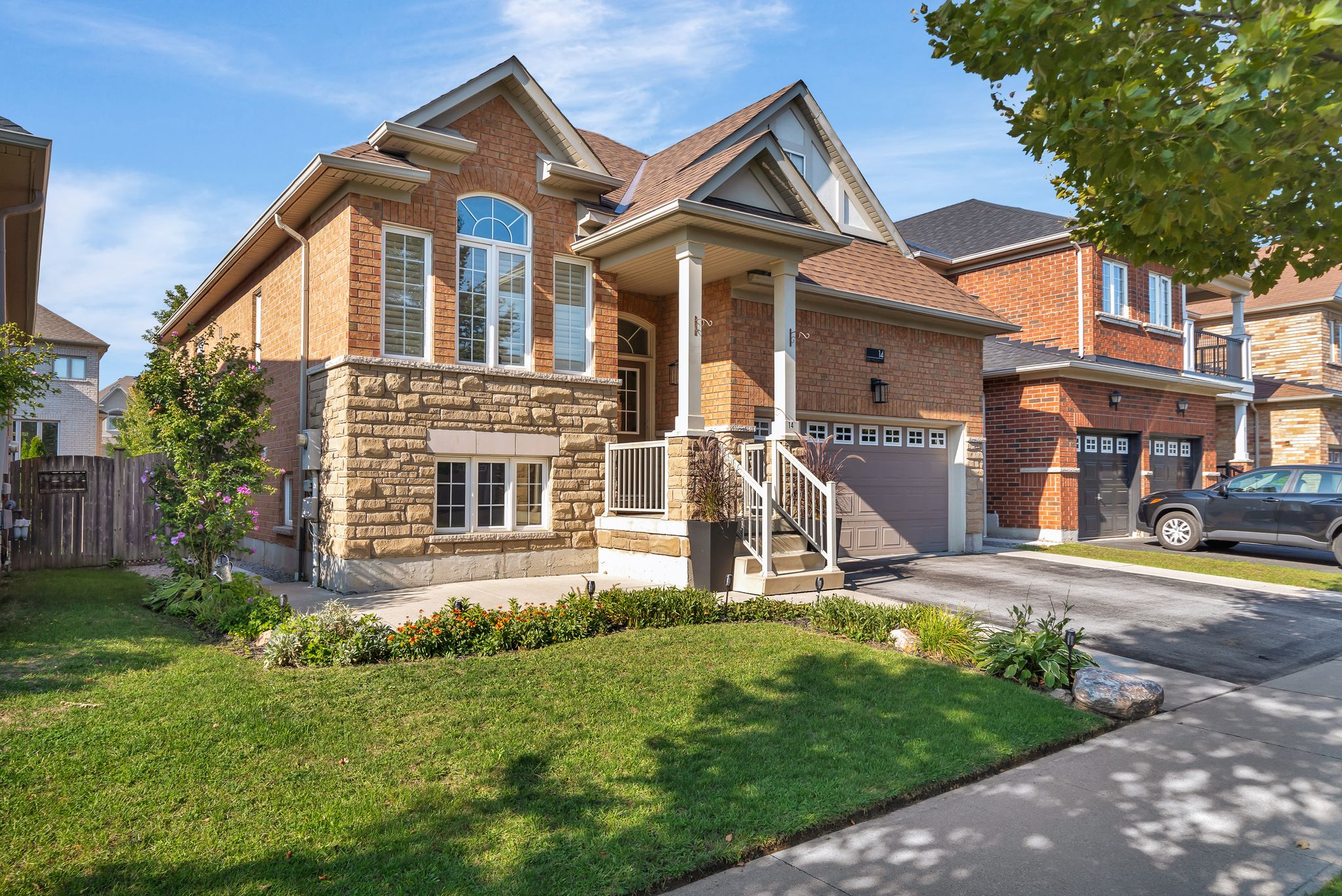 Front exterior view of 14 Sleepy Hollow Place, a raised brick and stone bungalow with a covered porch, double garage, and landscaped front yard, located on a quiet street in Whitby, Ontario.