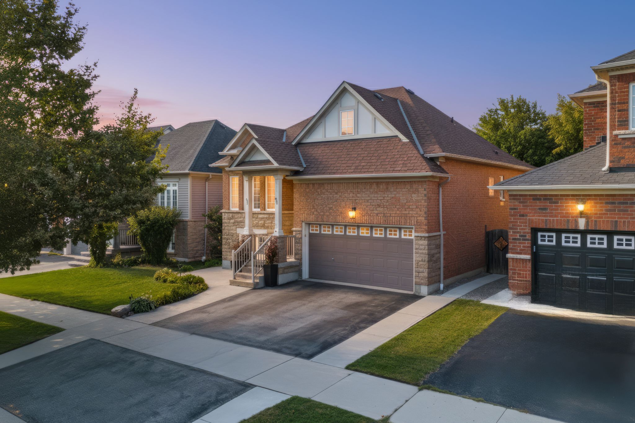 Front twilight exterior view of 14 Sleepy Hollow Place, a raised brick and stone bungalow with a covered porch, double garage, and landscaped front yard, located on a quiet street in Whitby, Ontario.