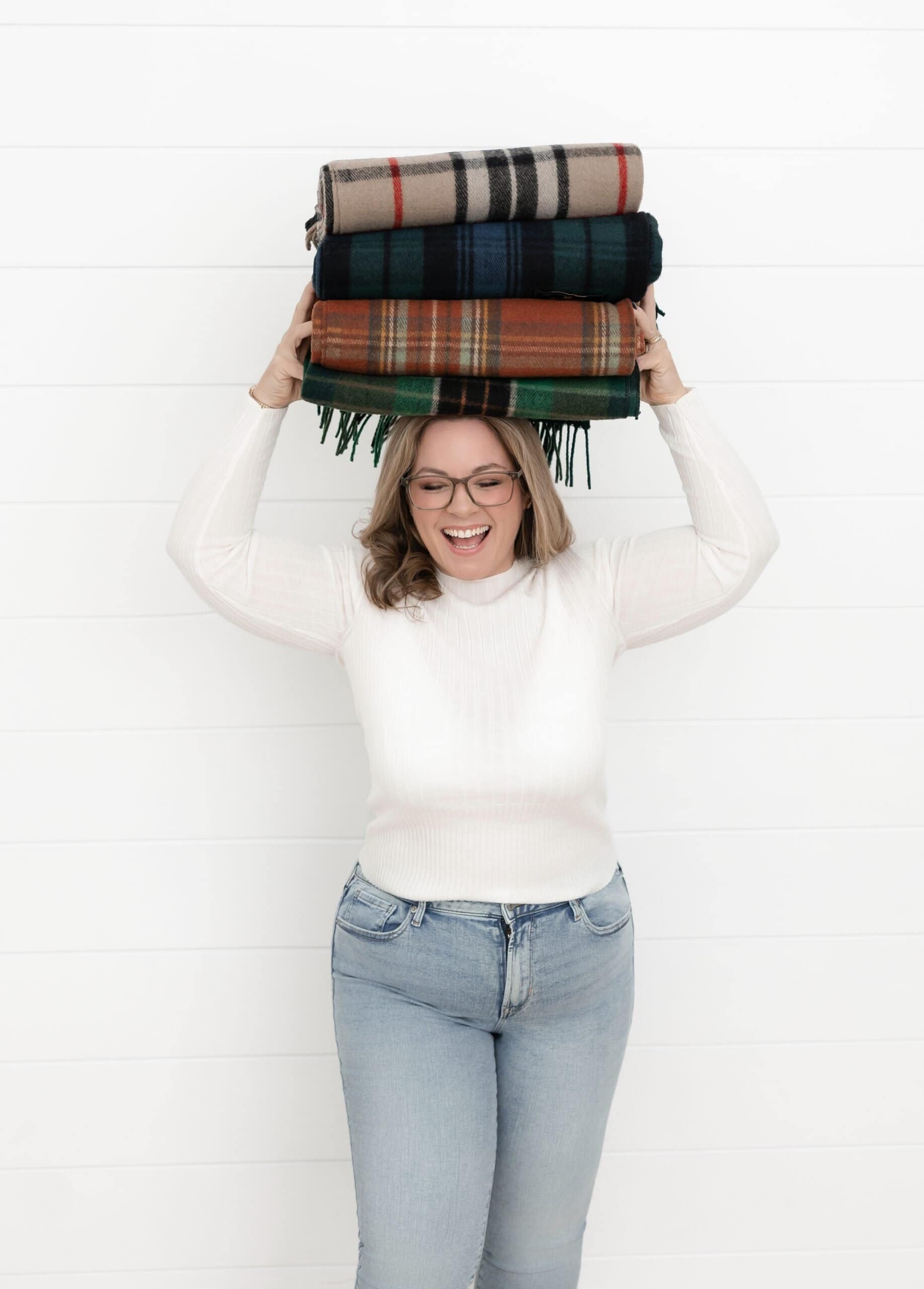 Laura McBride holding folded wool blankets, photographed in a bright, minimal studio setting.