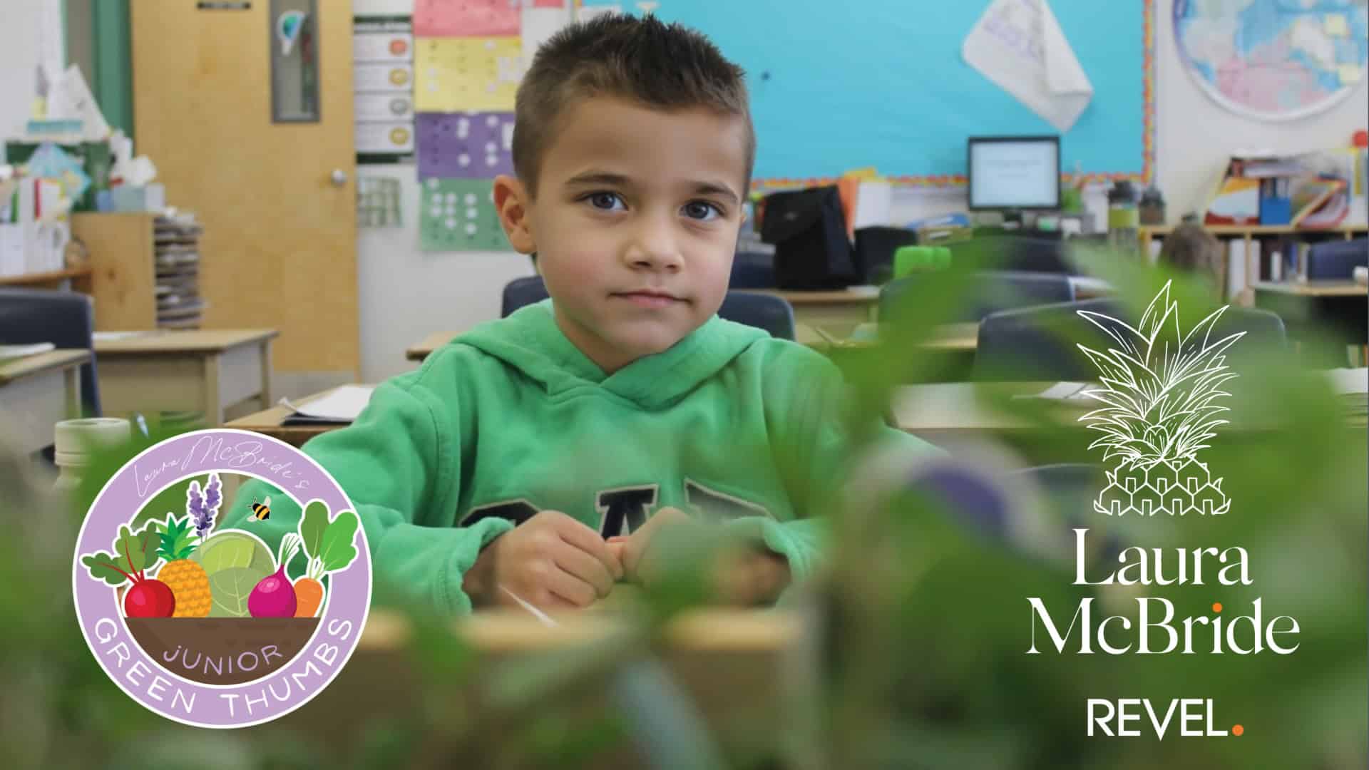 Young student sitting at a desk surrounded by plants in a classroom, part of the Junior Green Thumbs garden program supported by Laura McBride and Sutton Group