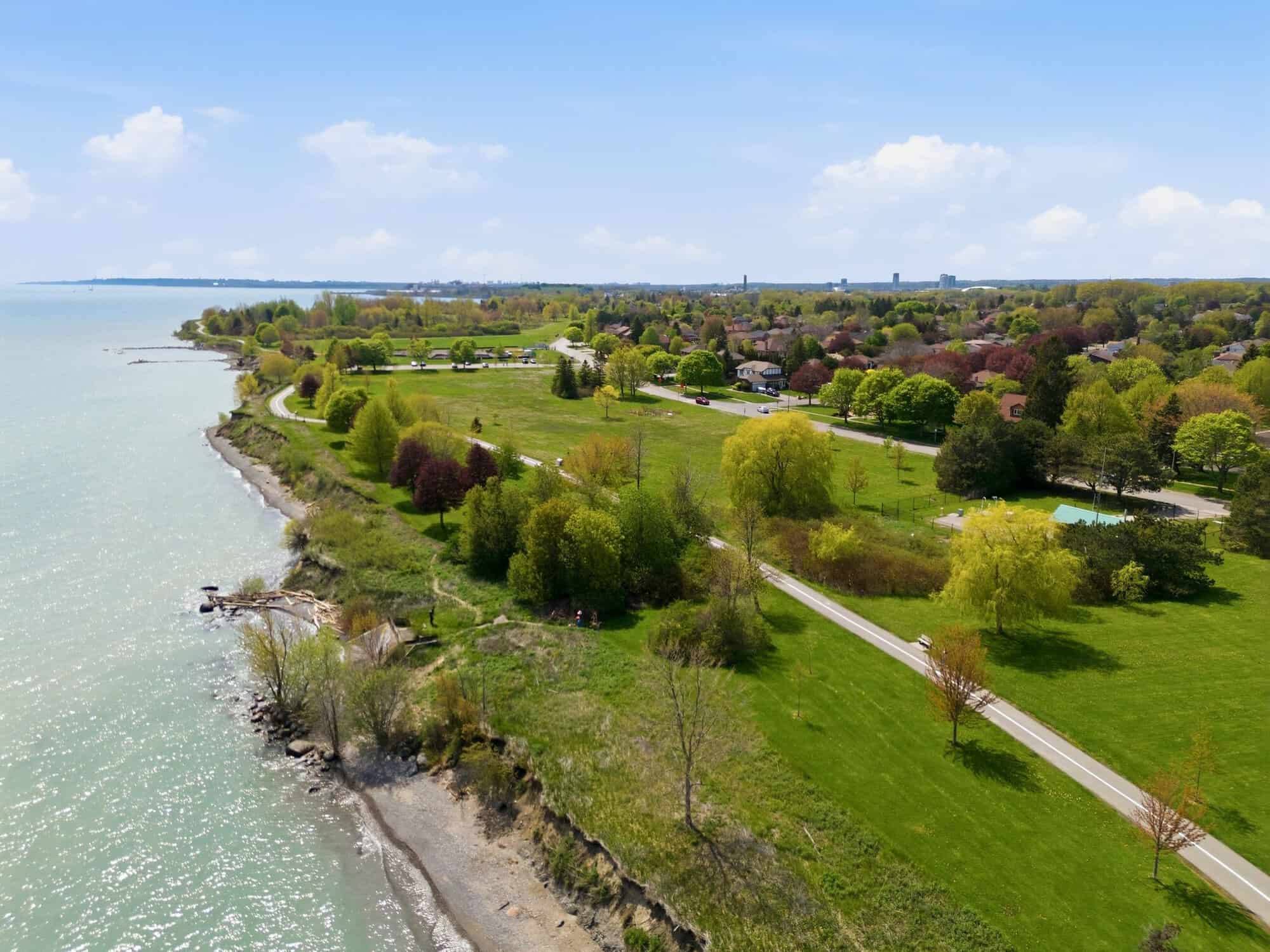 Elevated aerial view of an exclusive Lake Ontario waterfront neighbourhood in South Ajax, featuring luxury shoreline homes, estate properties, mature trees, expansive green space, and the surrounding countryside.
