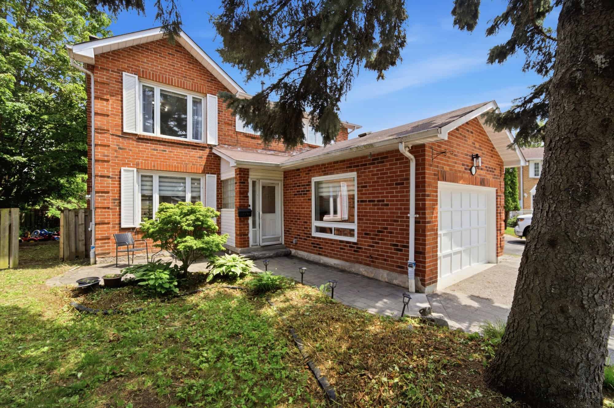 Daytime exterior of 13 Flowers Crescent in Ajax, a two-storey red-brick home with a former garage converted into a main-floor bedroom suite.