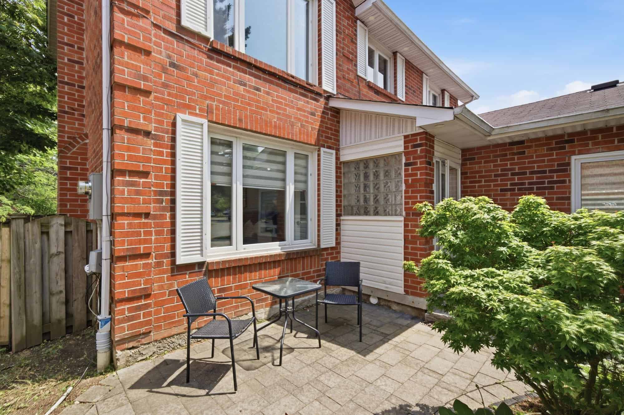 Small paved patio beside the front entrance of 13 Flowers Crescent in Ajax, with outdoor seating and mature landscaping.