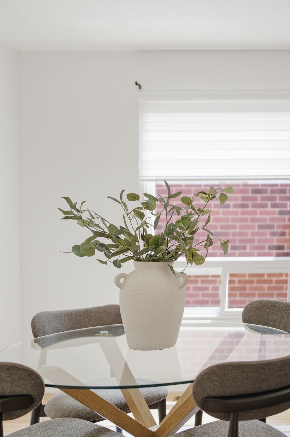 Close-up of the dining table at 13 Flowers Crescent in Ajax with a ceramic vase, greenery and upholstered chairs.
