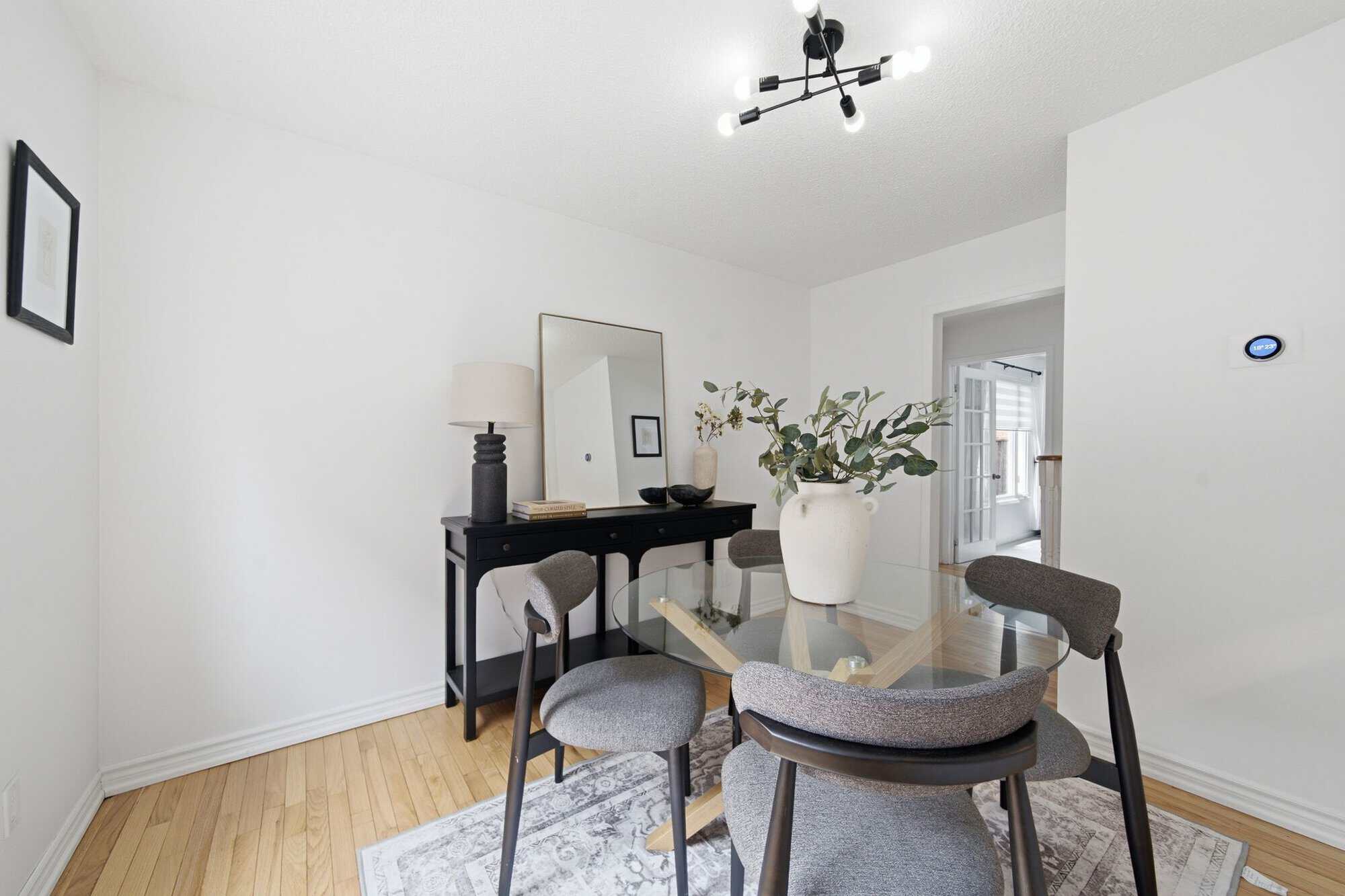 Dining room at 13 Flowers Crescent in Ajax with a round glass table, four upholstered chairs, hardwood floors and a black console.