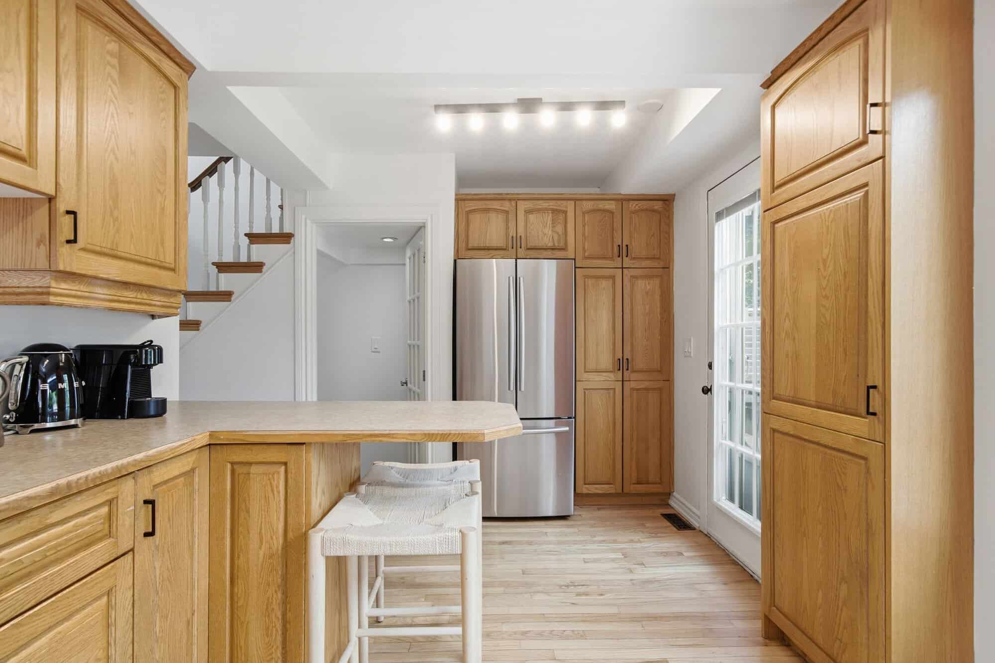 Kitchen at 13 Flowers Crescent in Ajax showing a stainless steel refrigerator, pantry cabinetry, breakfast bar and exterior door.