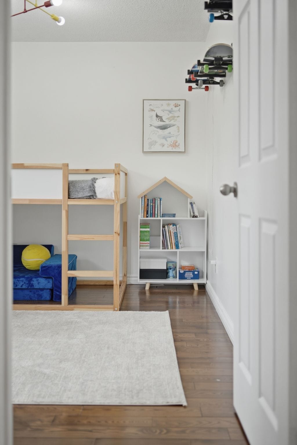 View into a children’s bedroom with a loft bed, blue play sofa, bookshelf and wall-mounted skateboards.