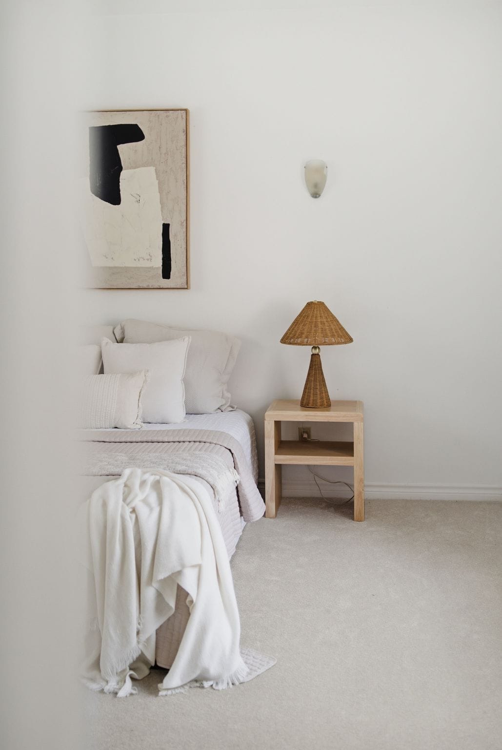 Bright main floor bedroom at 13 Flowers Crescent in Ajax with neutral bedding, abstract wall art, a wood nightstand and a woven table lamp.