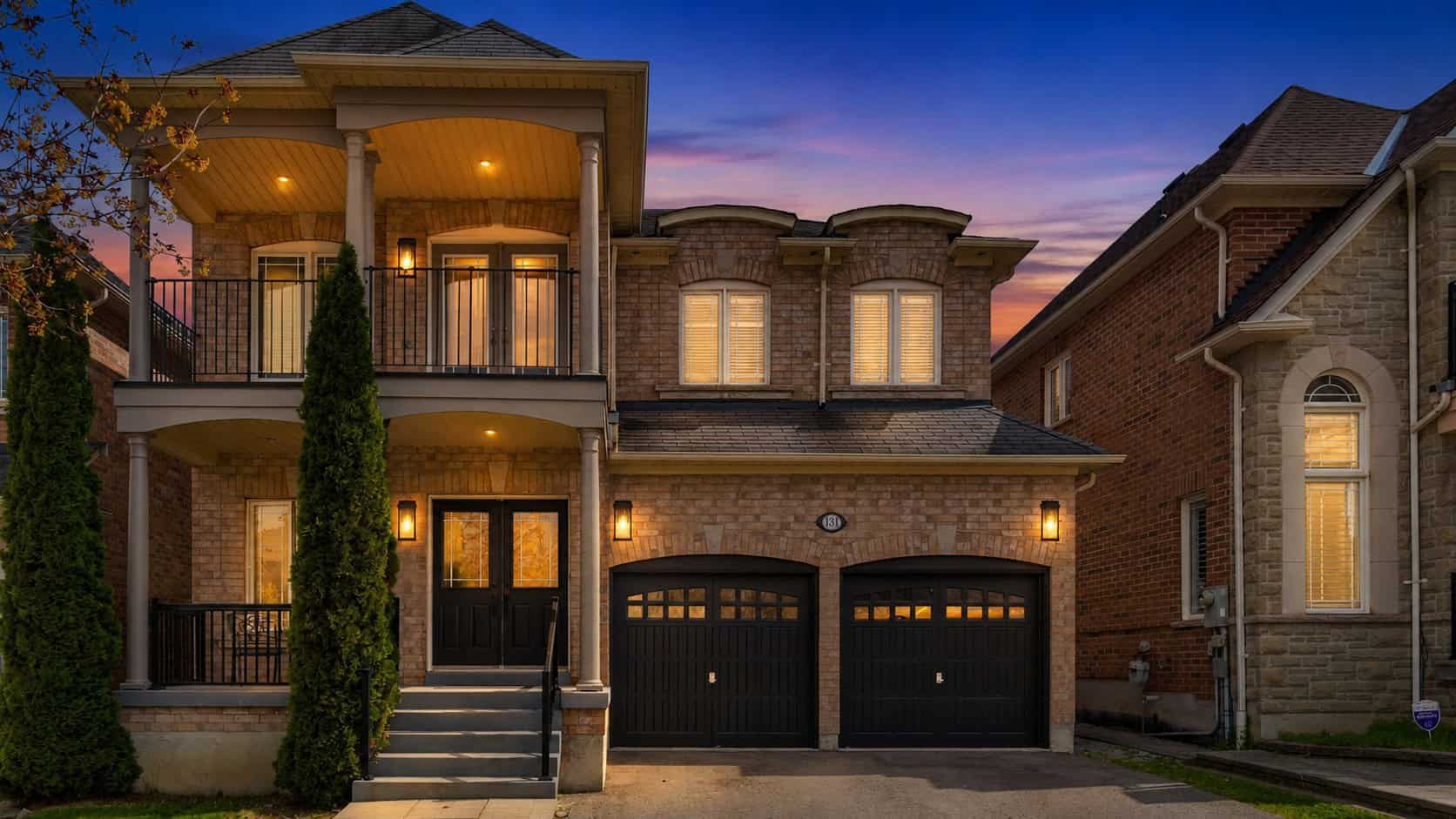 Exterior front view of 131 Rushworth Drive in Ajax with brick façade, covered porch, balcony, and double garage at twilight 