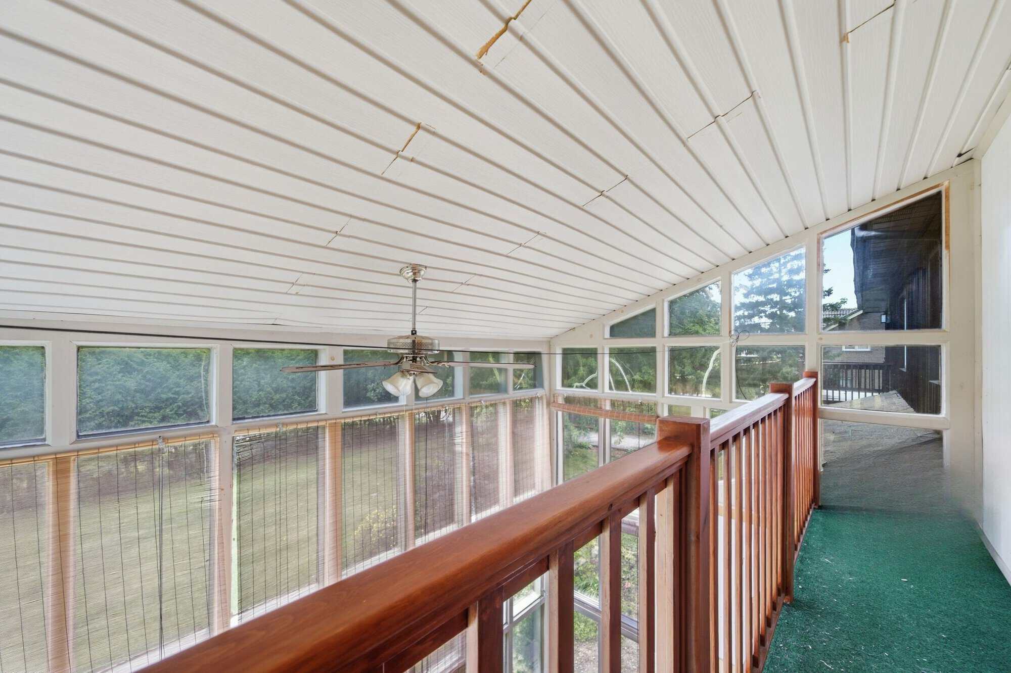 Upper interior balcony overlooking the sun-filled conservatory with panoramic windows and treetop views.