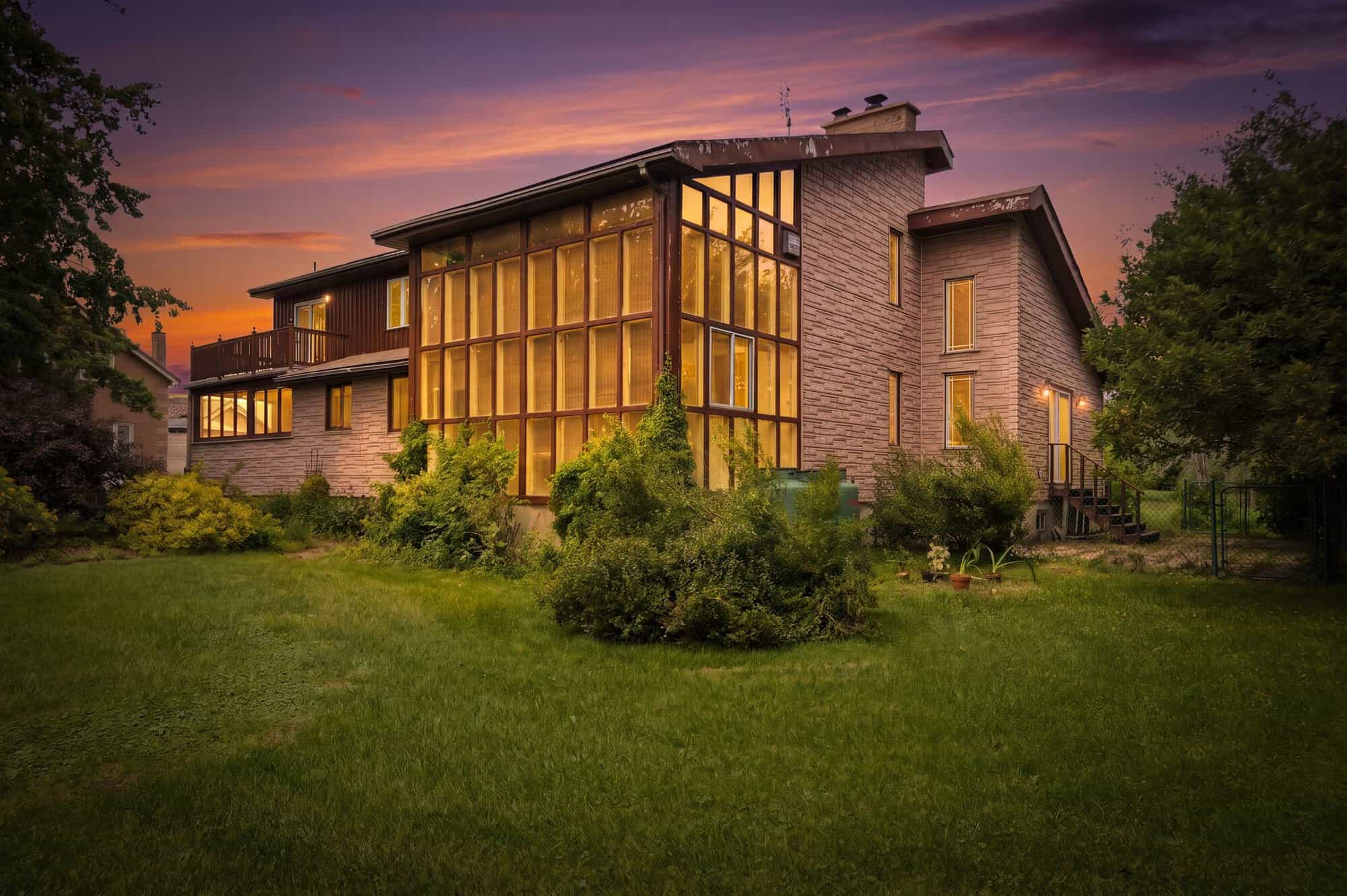 Rear exterior of 17 Ontoro Boulevard South in Ajax at dusk, featuring expansive windows, multiple levels, a balcony, and a spacious lawn.
