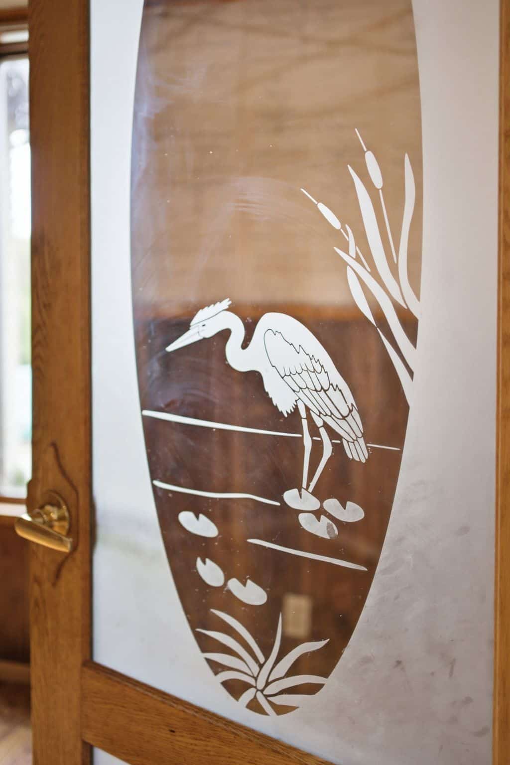 Decorative etched glass interior door featuring a heron and cattail design in a natural wood frame.