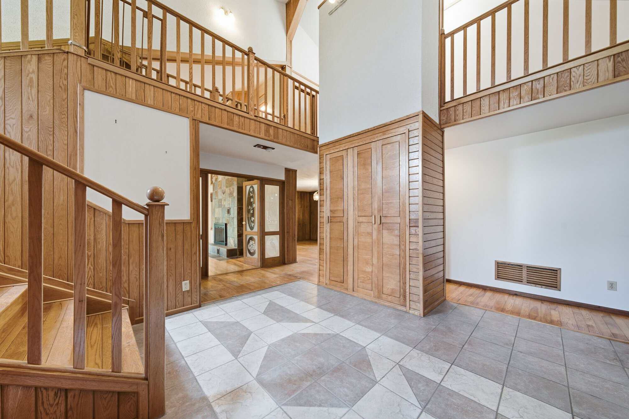 Grand two-storey foyer with open staircase, vaulted ceiling, upper gallery, tile flooring, and hardwood accents.