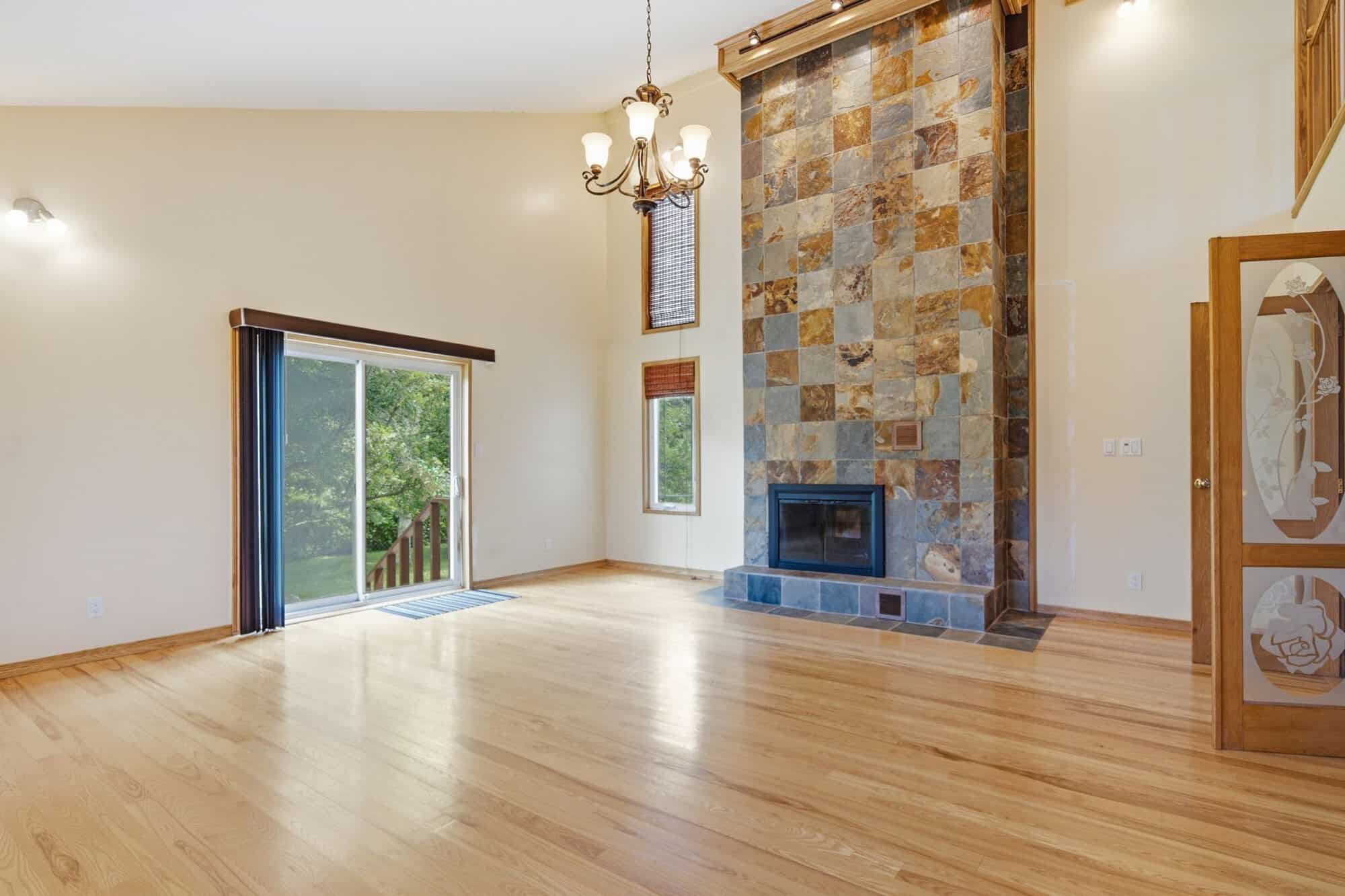 Spacious great room with vaulted ceilings, hardwood floors, oversized windows, and a dramatic floor-to-ceiling double-sided stone fireplace.