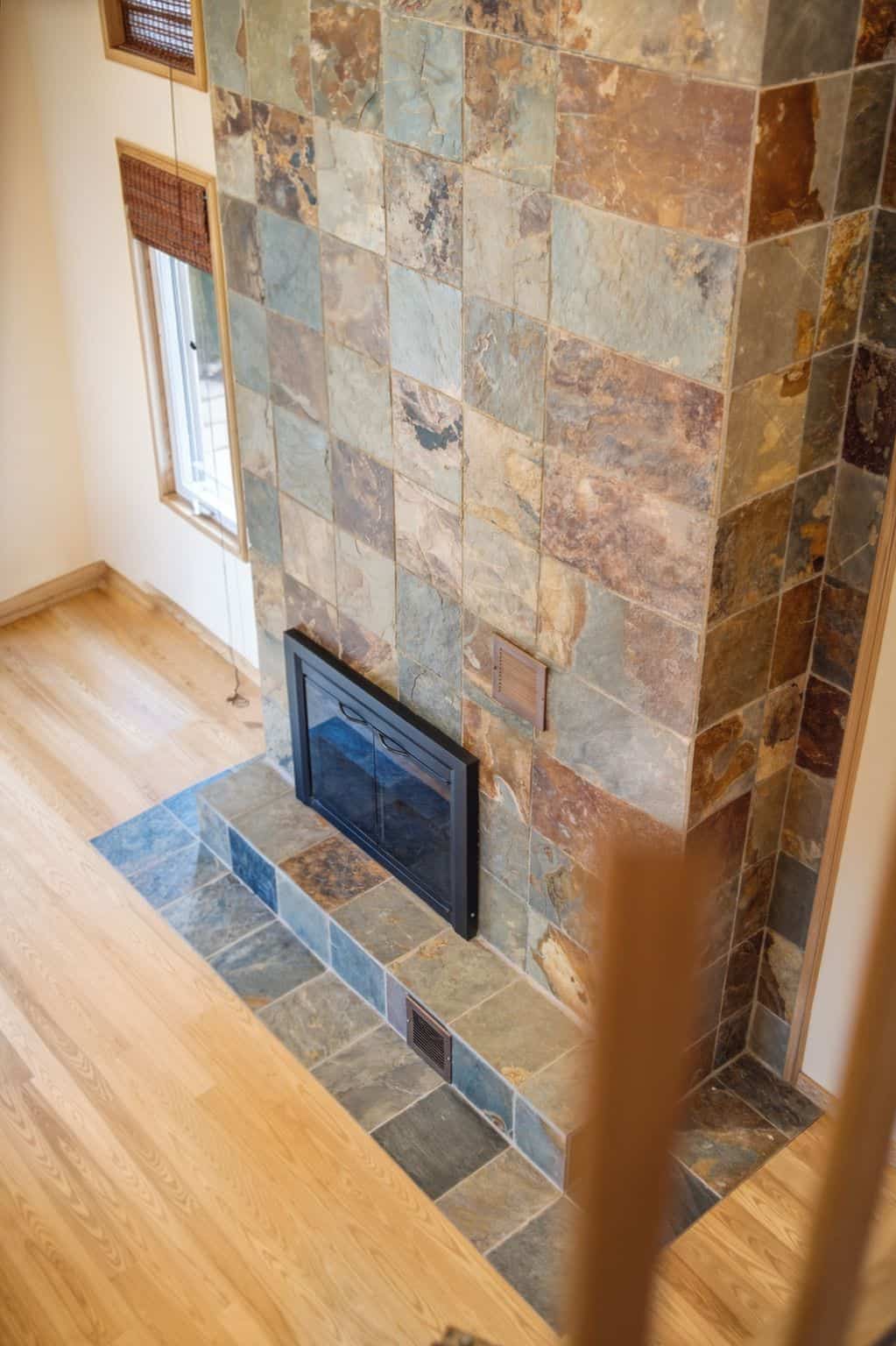 Spacious great room with vaulted ceilings, hardwood floors, oversized windows, and a dramatic floor-to-ceiling double-sided stone fireplace.