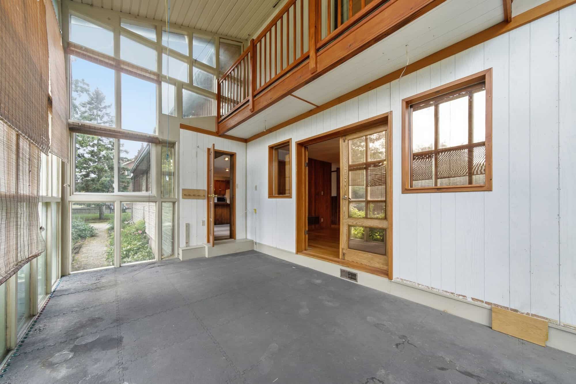 Bright three-season sunroom with soaring windows on three sides, vaulted ceiling, interior balcony above, and peaceful garden views.