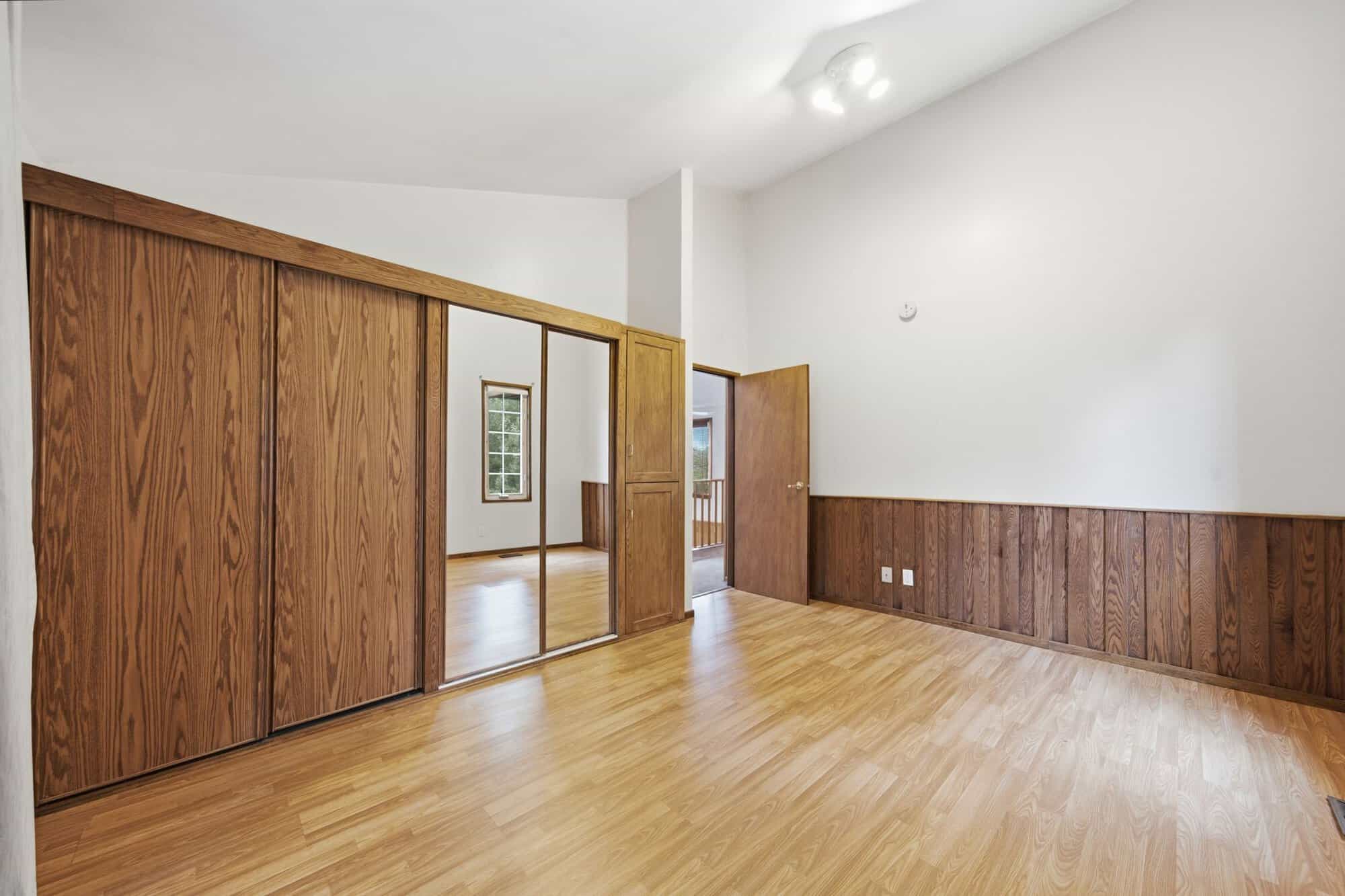Bright upper bedroom with vaulted ceiling, mirrored closet, and laminate flooring.