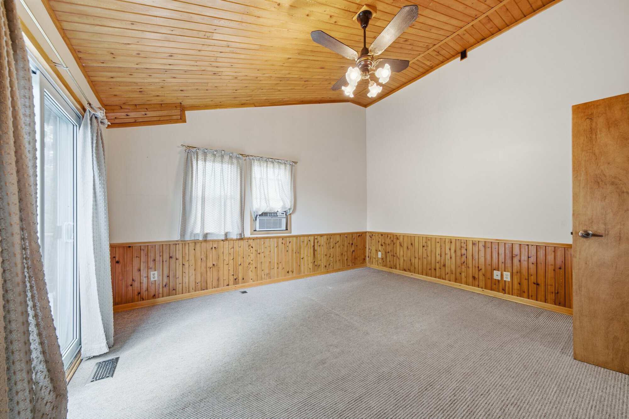 Bright primary bedroom with vaulted wood ceiling, private balcony access, and large open floor plan.