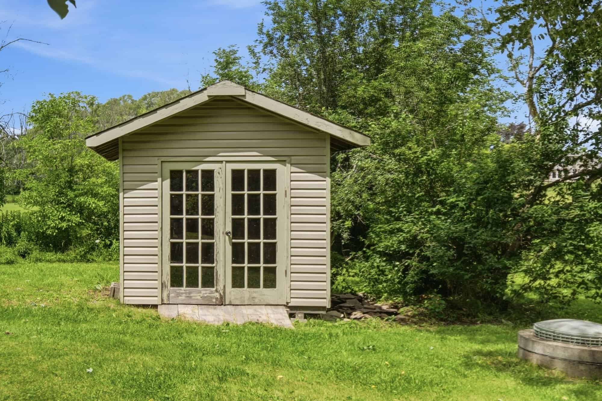 Detached garden shed with French doors set within the expansive backyard surrounded by mature trees.